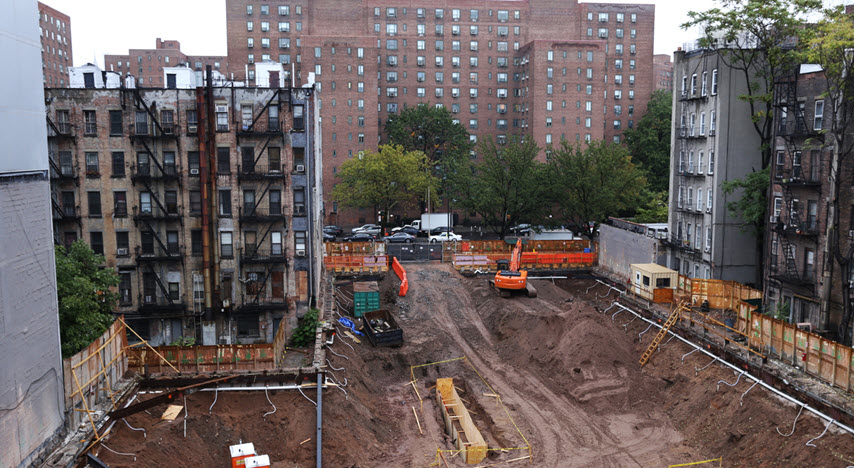 Picture of a construction site: tall buildings surrounding a large, open site that has been dug out.