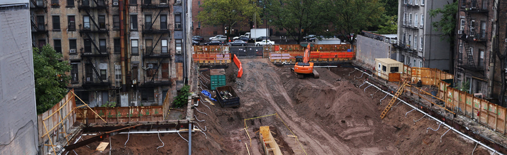 Picture of a construction site: tall buildings surrounding a large, open site that has been dug out.