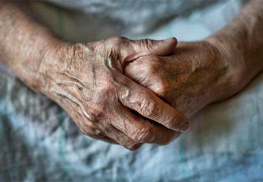 elderly person wearing hospital gown with hands folded over one another on their lap