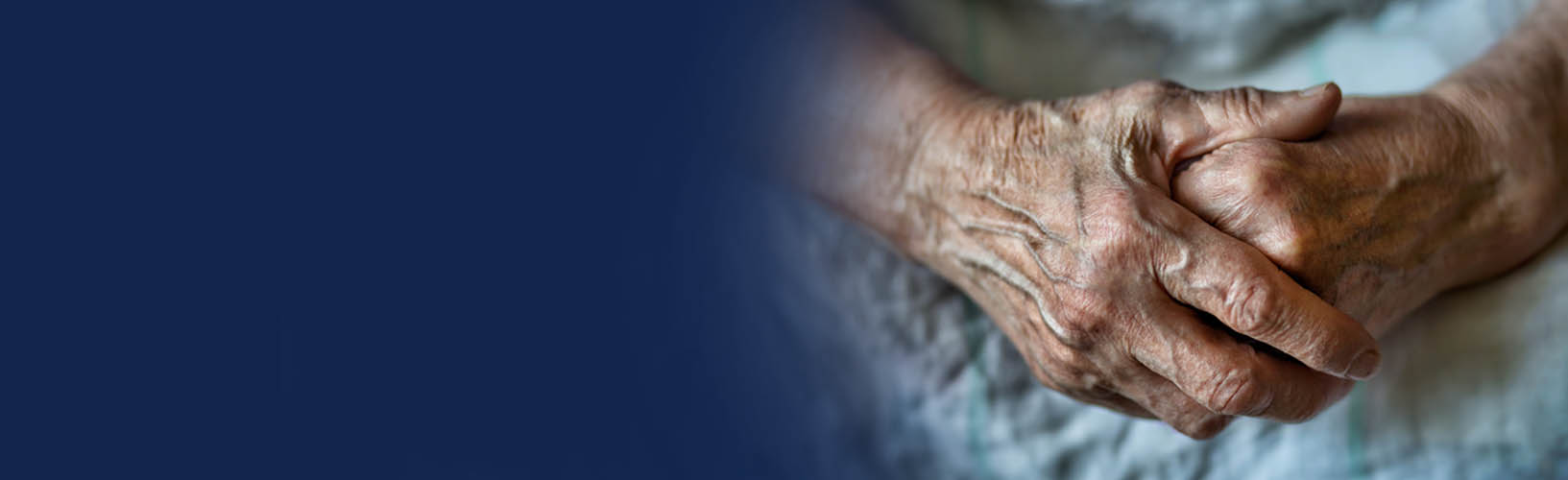elderly person wearing hospital gown with hands folded over one another on their lap