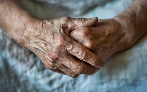 elderly person wearing hospital gown with hands folded over one another on their lap