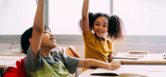 students sitting at desks with, each raising their hand
