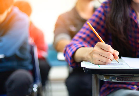 high school student sitting in a classroom writing with a pencil