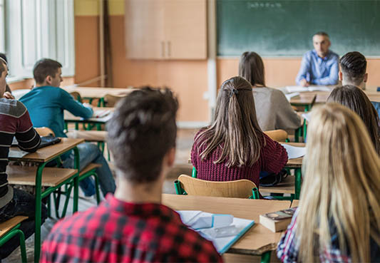 Students sitting at desks in a classroom looking at the teacher