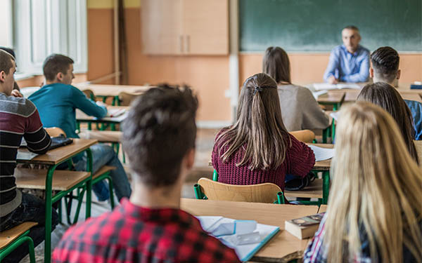 Students sitting at desks in a classroom looking at the teacher