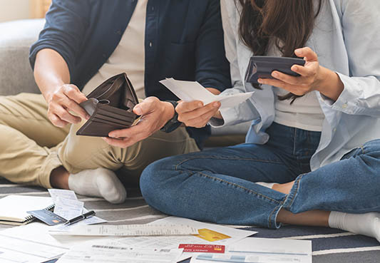 Young adults sitting on the floor holding wallets while looking at bills on the floor