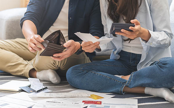 Young adults sitting on the floor holding wallets while looking at bills on the floor