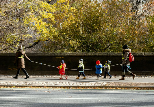 children walking in a line, holding a rope, between adults on each end of the rope