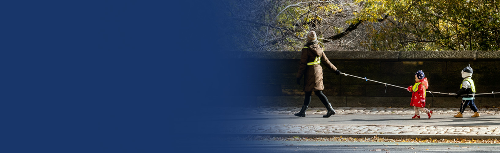 children walking in a line, holding a rope, between adults on each end of the rope