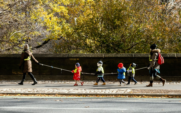 children walking in a line, holding a rope, between adults on each end of the rope