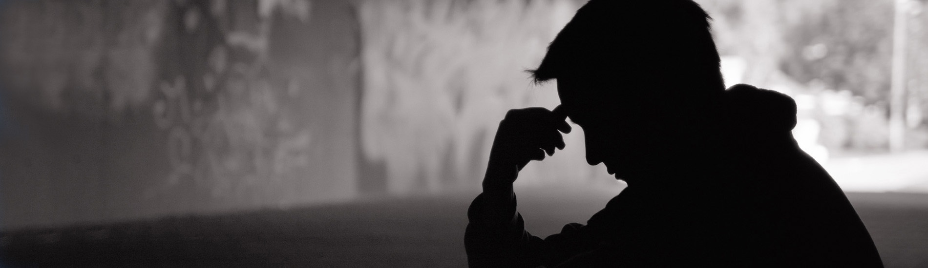 Man sitting in a bridge tunnel looking distressed.