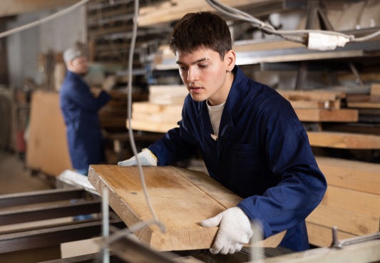 Young person working on a table saw in a commercial woodshop.