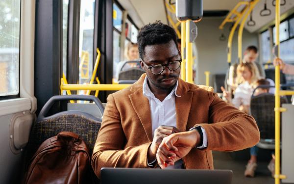man checks the time on his watch as he sits on the bus