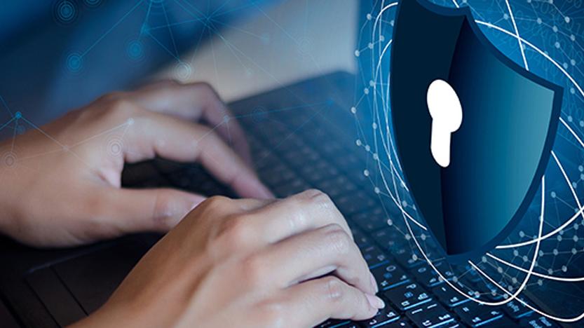 A woman types on a computer keyboard with the graphic image of a lock and shield hovering above her computer screen.