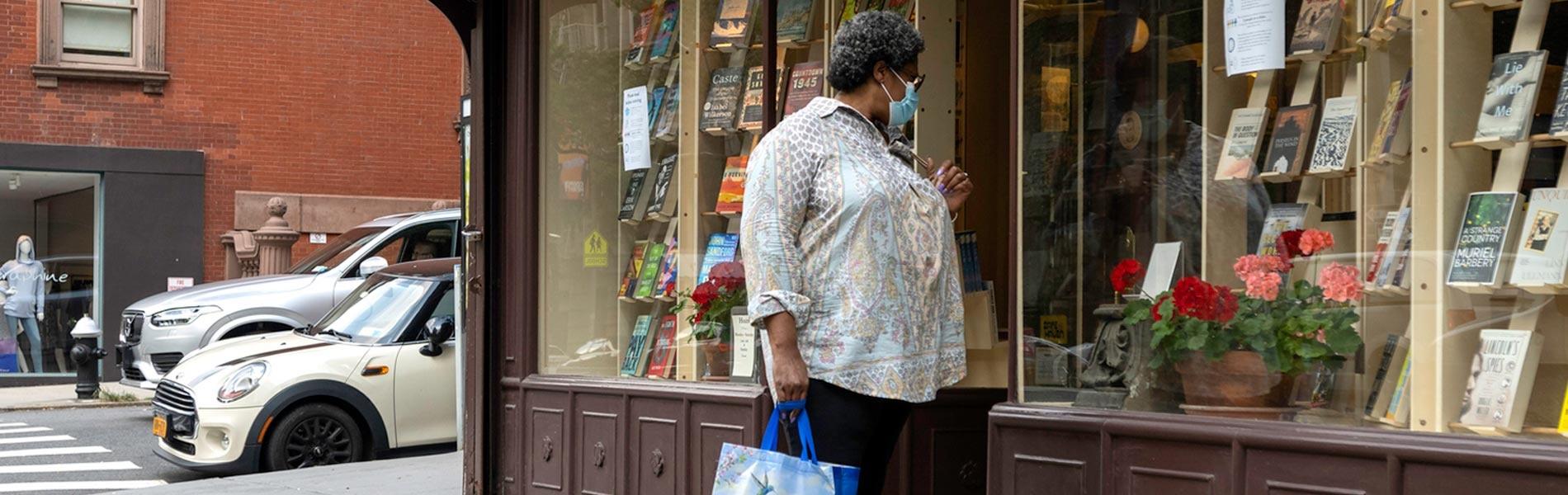 Woman wearing face mask looking at window display of bookstore.