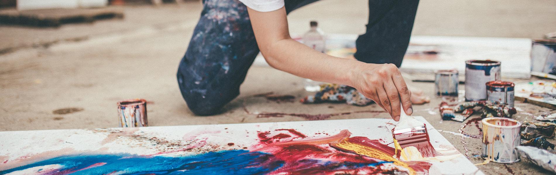 Artist painting on a canvass on a floor.