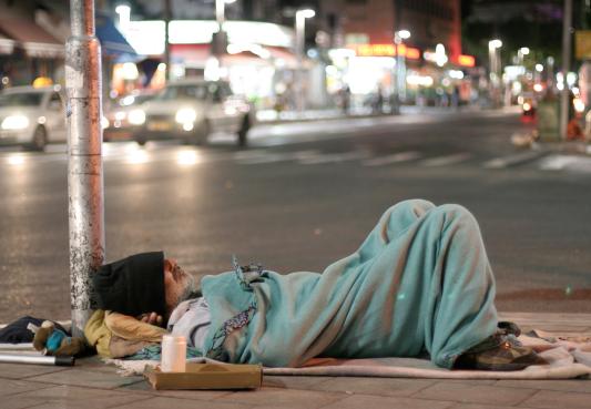 a man experiencing homelessness sleeping on a busy sidewalk