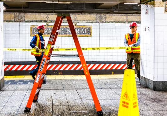 construction worker inspecting leak in underground transit empty large platform in new york city subway station in grand central