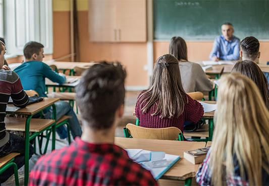 Students sitting at desks in a classroom looking at the teacher