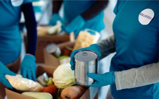 volunteer at food pantry packing boxes of groceries in an assembly line of other volunteers