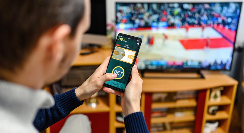 person using phone to place bet while watching television