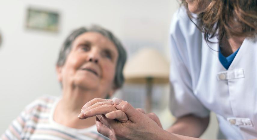 Elderly person's hand being held by a care giver.