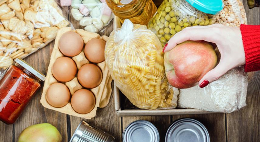 Different food items displayed on a table with a hand holding an apple