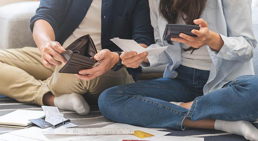 Young adults sitting on the floor holding wallets while looking at bills on the floor